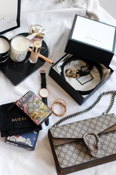 the contents of a gucci handbag are laid out on a white bed sheet