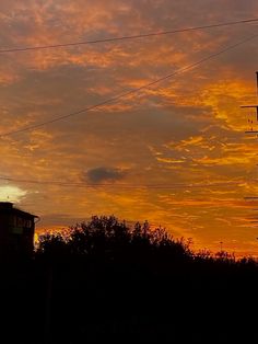 an orange and yellow sky with power lines in the foreground, trees to the right