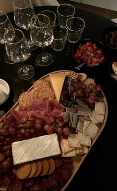 a platter of cheese, crackers, and grapes on a table with wine glasses