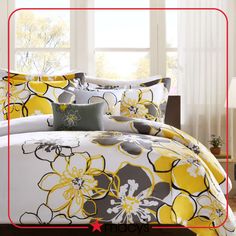 a bed with yellow and gray flowers on it in front of a white curtained window