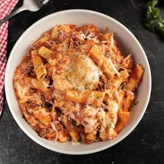 a white bowl filled with pasta and sauce on top of a black table next to a red checkered napkin