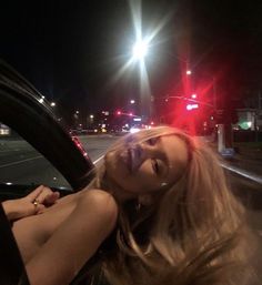 a woman sitting in the driver's seat of a car at night with traffic lights behind her