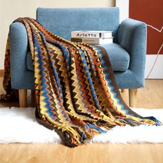 a couch with a blanket on top of it next to a book and a chair