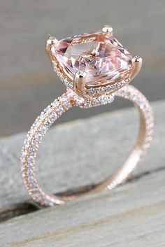 an engagement ring with a pink morganite surrounded by pave diamonds on a wooden surface