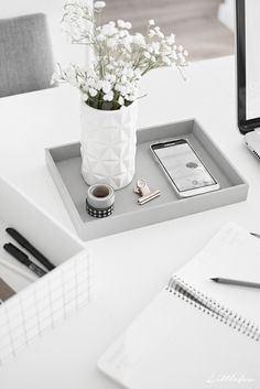 a white vase with flowers on a tray next to a laptop computer and notebooks