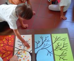 three children are sitting on the floor and painting trees with colored paper, while another child is standing in front of them