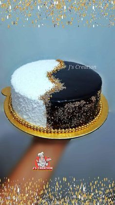 a black and white cake with gold sprinkles on the top is being held by a hand