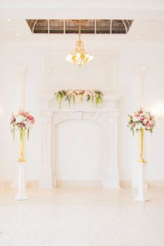 a room with white walls and flowers on the fireplace mantels in front of it