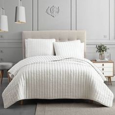 a bed with white comforter and pillows in a gray room next to a lamp