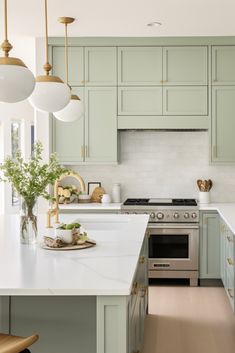 a kitchen with green cabinets and white counter tops, gold accents on the ceiling lights