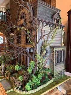 a doll house with trees and bushes in front of it