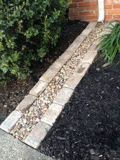 a brick walkway next to a bush and shrubbery on the side of a building