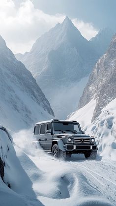 a mercedes benz g - class driving through the snow in front of some mountain peaks