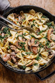 a skillet filled with pasta, mushrooms and spinach on top of a wooden table