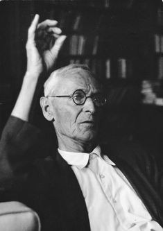 an old man sitting in a chair with his hand up to the ceiling and looking off into the distance