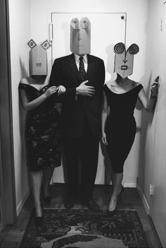 three people standing next to each other in front of a mirror with paper masks on their heads