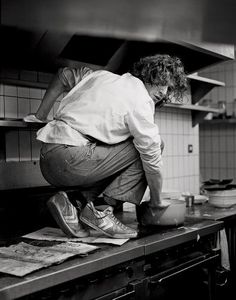 black and white photograph of a man leaning over the counter in a kitchen with pots on it