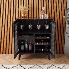 a black cabinet with wine glasses and bottles on it next to a potted plant