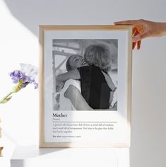 a person holding up a framed photo in front of a vase with flowers