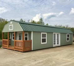 a small green and white house with a porch on the front, sitting in a parking lot