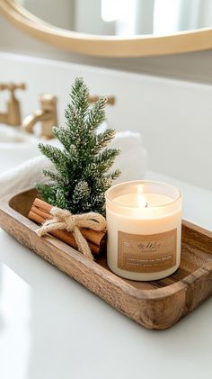 a candle and some cinnamon sticks on a tray in front of a mirror with a christmas tree