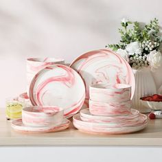 pink and white marble dinnerware set with flowers in vase behind it on wooden table