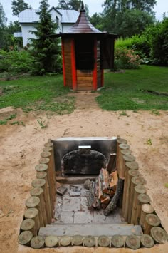 an open fire pit sitting in the middle of a dirt field next to a building