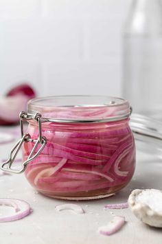 a jar filled with red onions sitting on top of a white counter next to sliced onions