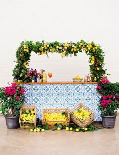 a table topped with lemons and flowers next to baskets filled with yellow fruit on top of a tiled counter