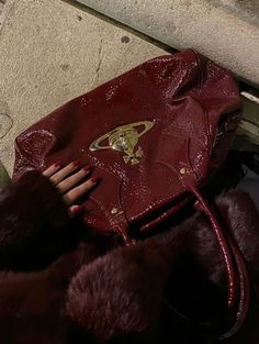 a woman's hand holding onto a red purse on top of a stone bench