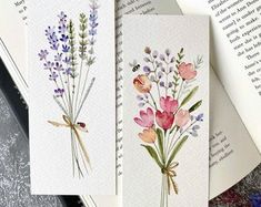 three cards with watercolor flowers on them and an open book in the back ground