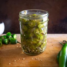 a jar filled with pickles sitting on top of a wooden table next to green peppers