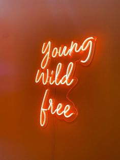 a neon sign that says young wild free on the side of a wall with an orange background