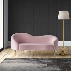 a pink couch sitting on top of a hard wood floor next to a tall lamp