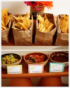 some food is sitting in small bowls on a table and there are chips, salsa, guacamole