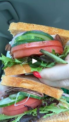 a hand holding a sandwich with lettuce, tomato and cucumber