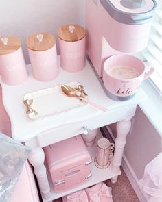 pink kitchen accessories and utensils are arranged on a small white table in front of a window