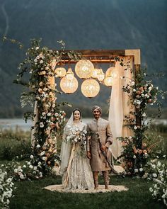 a man and woman standing in front of a floral arch