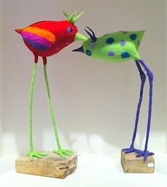 two colorful birds standing next to each other on top of a wooden block in front of a white wall