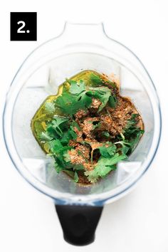 a blender filled with green vegetables on top of a white table