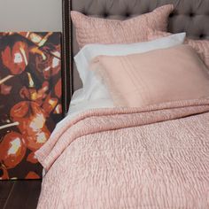 a bed with pink sheets and pillows on top of it next to a framed painting