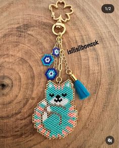 a cross stitch keychain with a blue cat on it's side and a tassel hanging from the front