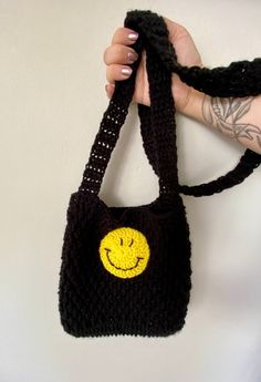 a hand holding a black crocheted bag with a smiley face on it