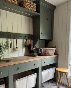 a kitchen with green cabinets and white baskets on the counter top, next to a wooden stool