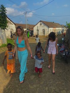 a woman walking down a dirt road holding hands with two small children and an adult