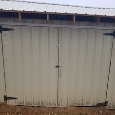 the side of a metal building with two doors and some dirt on the ground next to it