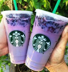 two starbucks drinks with blueberries and yogurt in them are being held by someone's hands