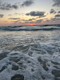 the sun is setting over the ocean with footprints in the sand and waves coming ashore