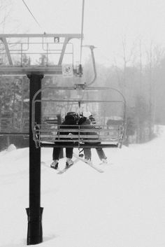 two skiers are sitting on a ski lift above the snow covered ground in black and white