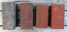 four bricks lined up in a row on a wooden surface, one red and one grey